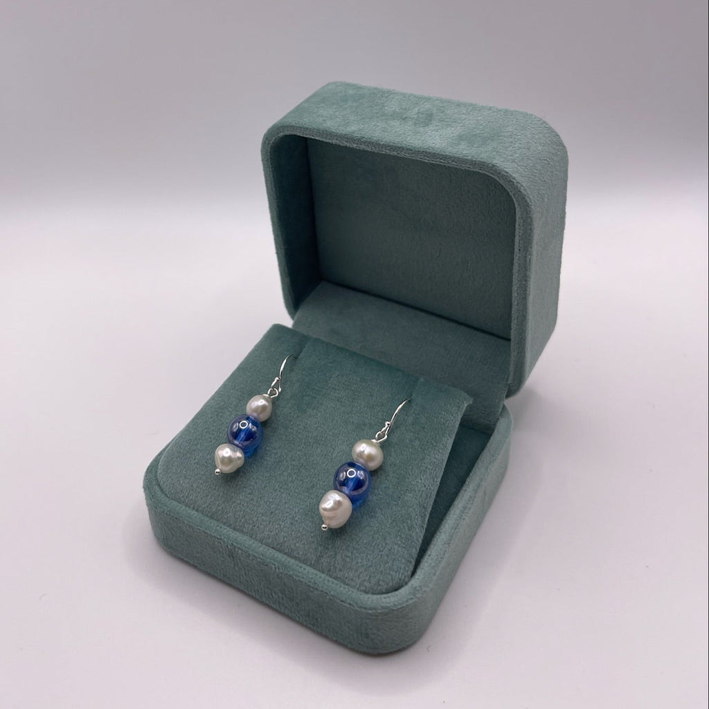 Pair of earrings with blue and white pearls on a light gray background