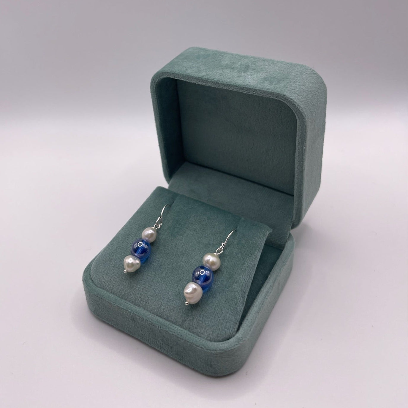 Pair of earrings with blue and white pearls on a light gray background