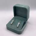 Teal jewelry box with pearl earrings on a light gray background