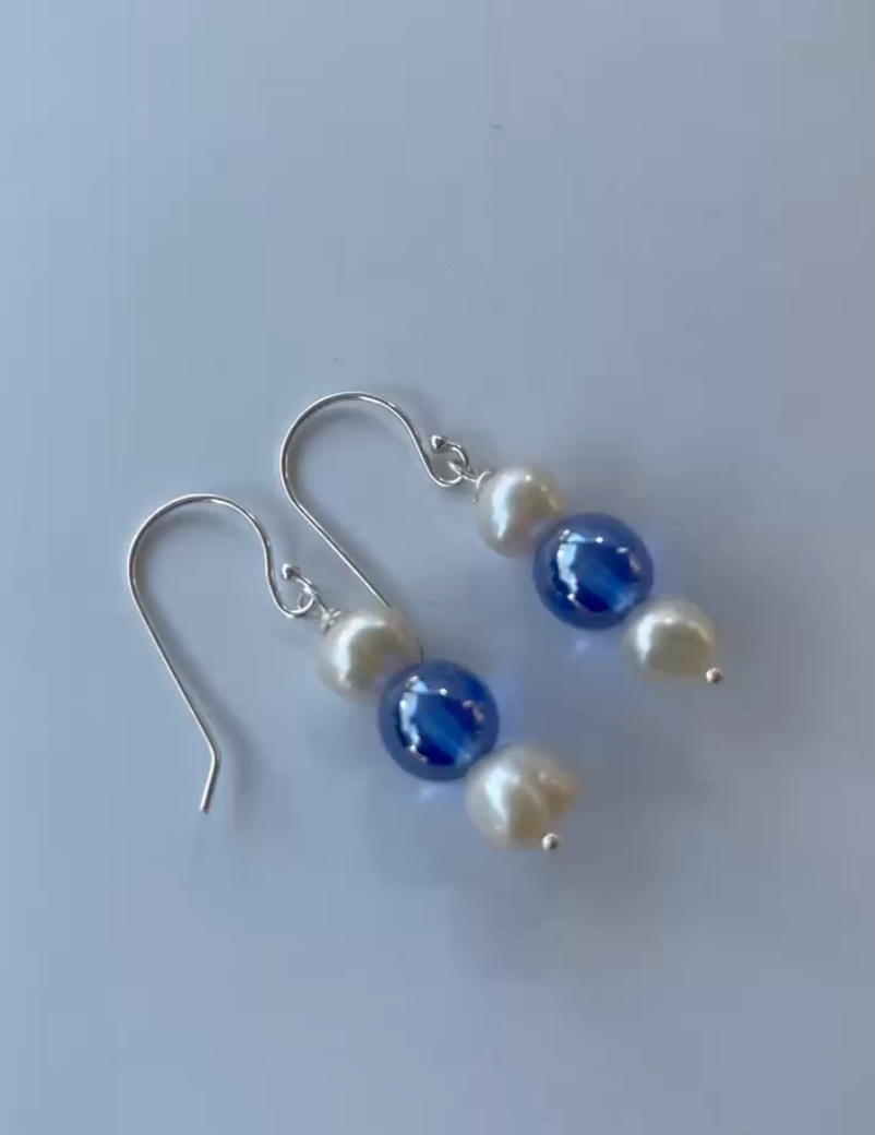 Pair of earrings with blue and white pearls on a light gray background